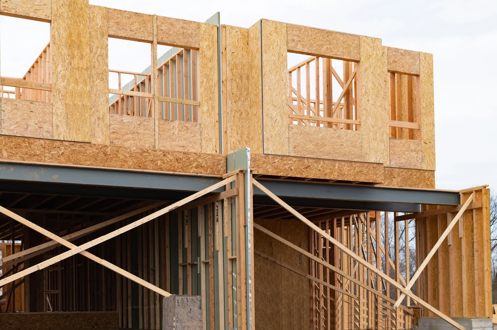 A partially constructed building with wooden framing and oriented strand board walls, showing open window spaces and exposed structural beams—ideal for estimating second story addition cost.